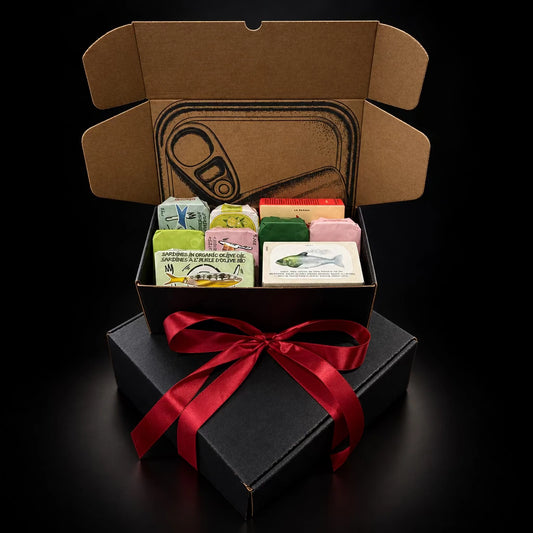 Tinned fish mystery box, open with assorted sardine and seafood tins, on a black gift box with red ribbon