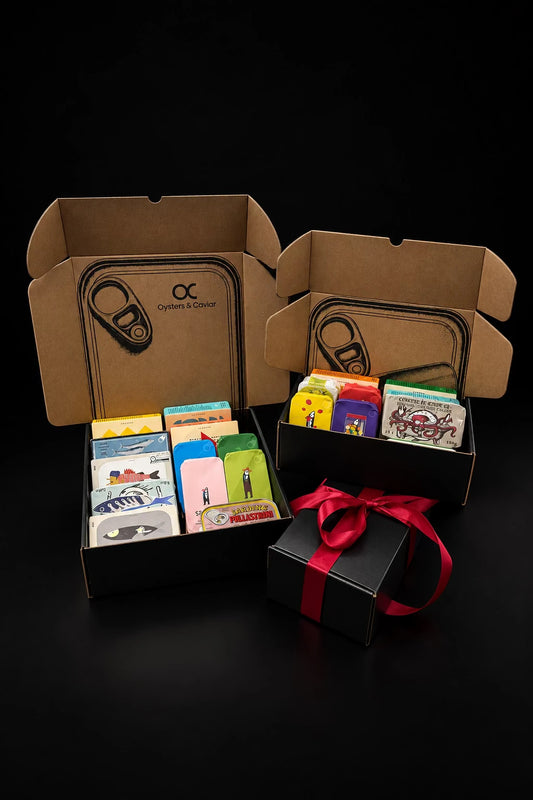 Two open Oysters & Caviar tinned fish mystery boxes, large and small, with a black gift box and red ribbon